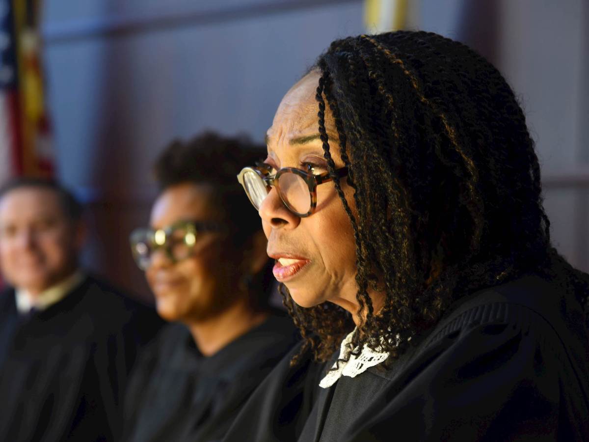 A profile of Joy Cunningham, a Black female supreme court justice, wearing a black robe and glasses with two other justices seated behind her.