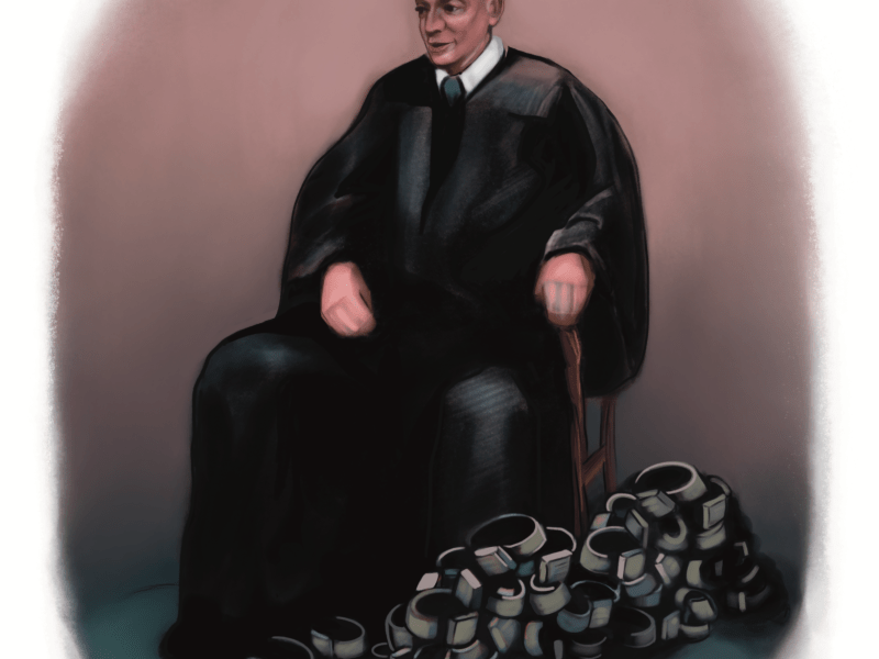 A judge in a Black robe with a pile of SCRAM bracelets at his feet