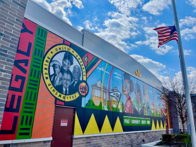 A colorful mural with faces of Black Americans and words including "legacy," "pride," "unity," "fellowship," "peace," and "community".